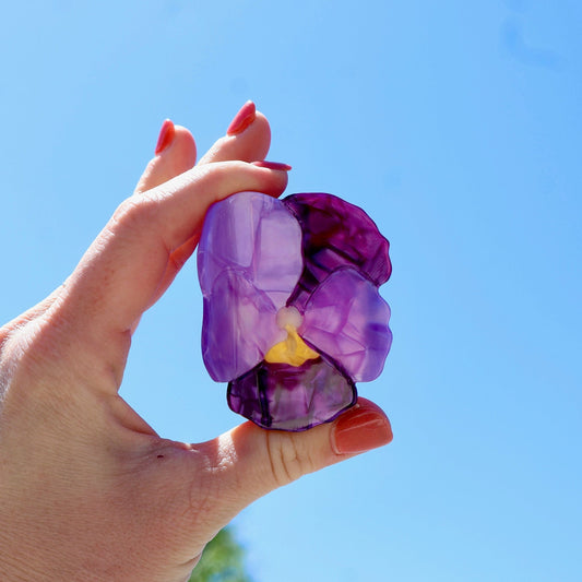 Hand holding a purple flower against a clear blue sky