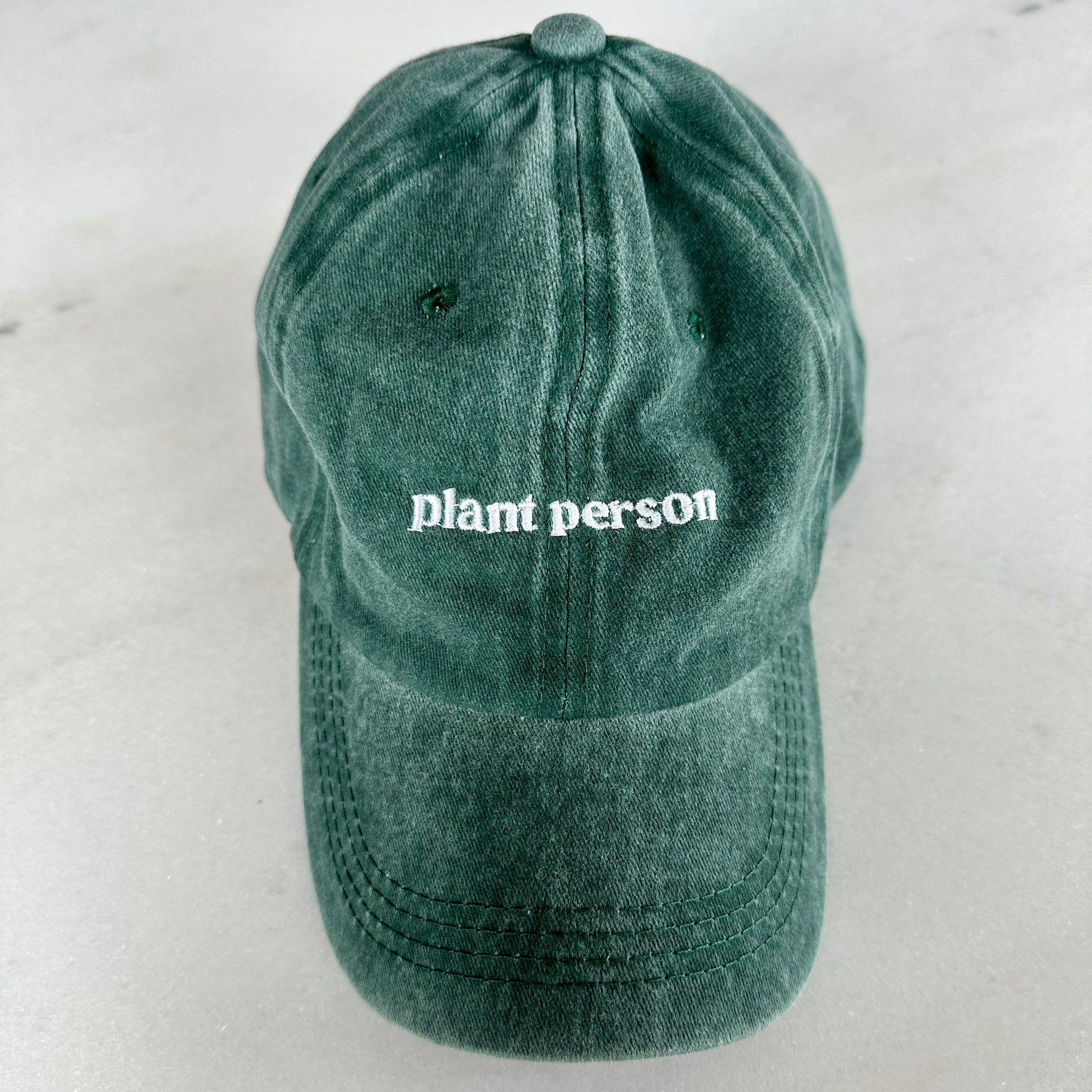 Top view of a washed green denim dad cap that says plant person in white serif font