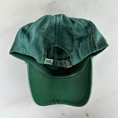 Back view of washed dark green baseball cap with a brass metal buckle and tag that says "bittergoods"