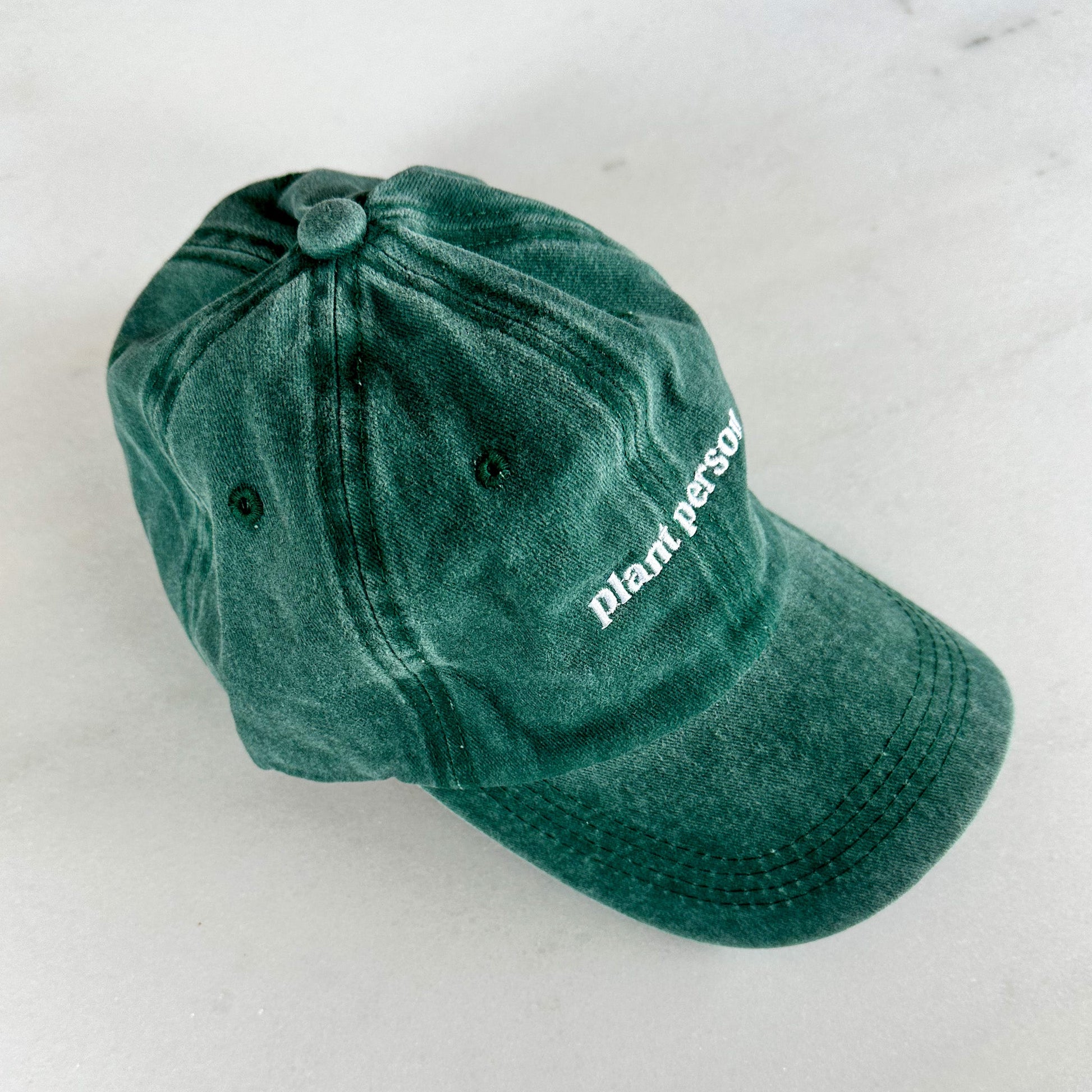 Pictured from the left, a washed green denim dad hat that says plant person in white font