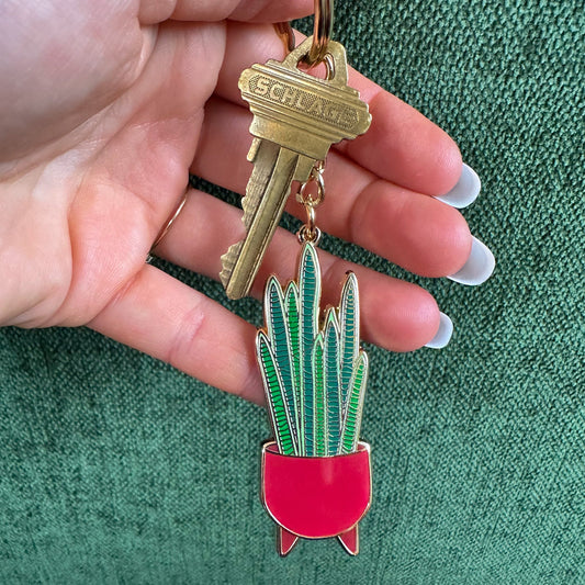 Snake plant keychain on a key ring with a gold key held by manicured hand on green background